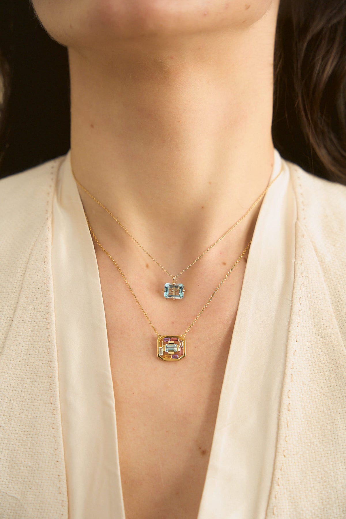 Model's neck wearing two 18K yellow gold necklaces from Nayestones, Belgian fine jewelry. The first is the Octogone Necklace featuring a big octogonal blue topaz, and the second is the Art Deco Aura Necklace, featuring a central octogonal blue topaz surrounded by baguette-cut tourmalines, citrines, amethysts and blue topaz.