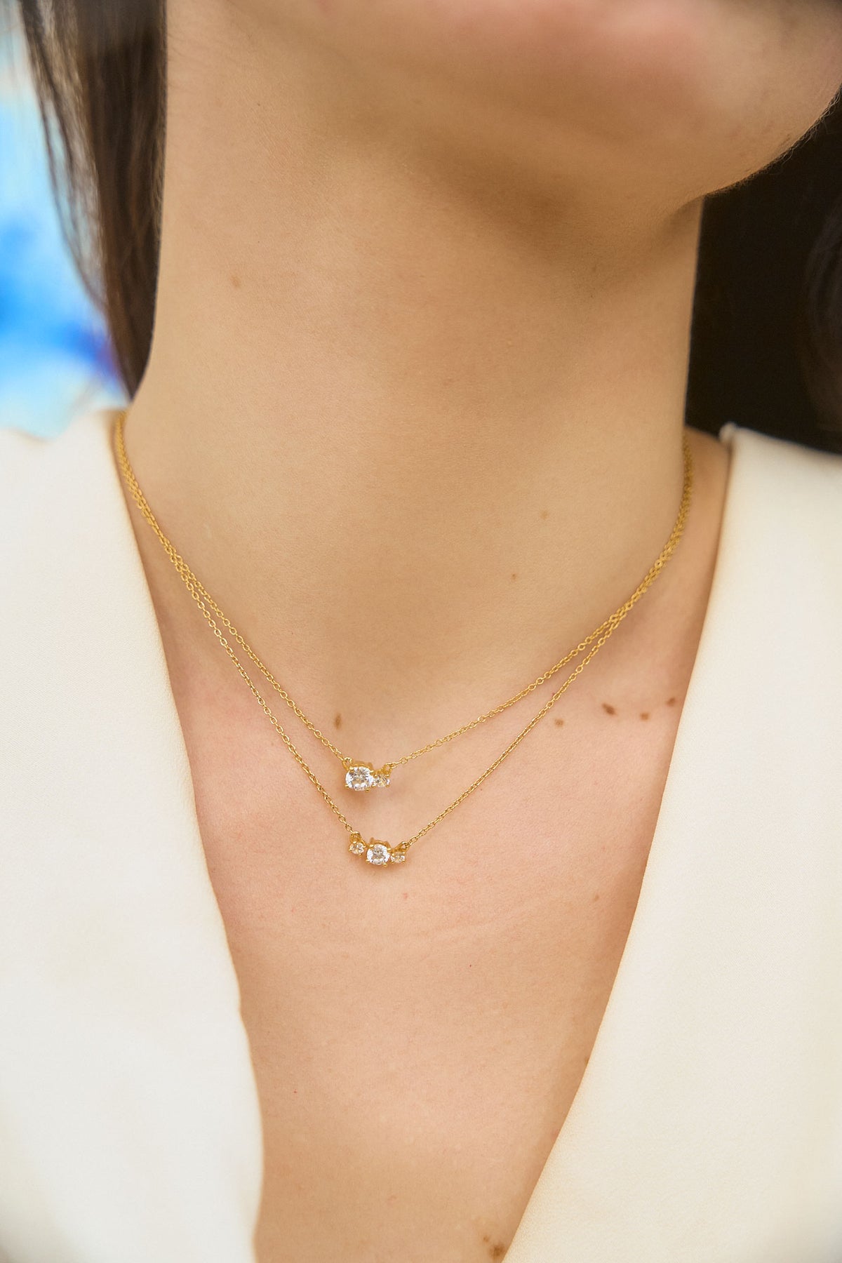 Woman wearing two yellow gold necklaces set with two and three diamonds of different sizes, from the Essential collection by Nayestones. Fine, luminous jewelry worn on bare skin in natural light.