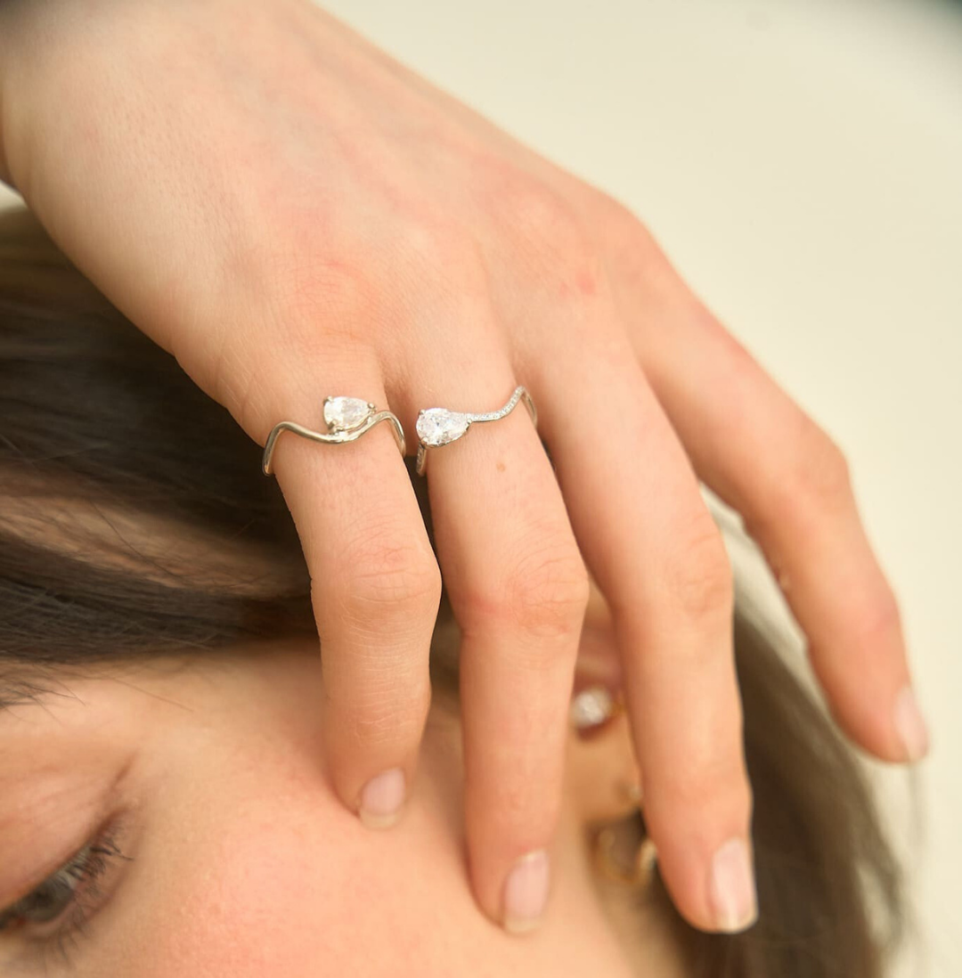 Feminine hand wearing an 18-carat white gold ring adorned with a 0.25-carat pear-shaped horizontal diamond, and a diamond-paved white gold ring with a 0.7-carat central diamond. The mood is natural and luminous, reflecting Nayestones' minimalism and modern elegance.