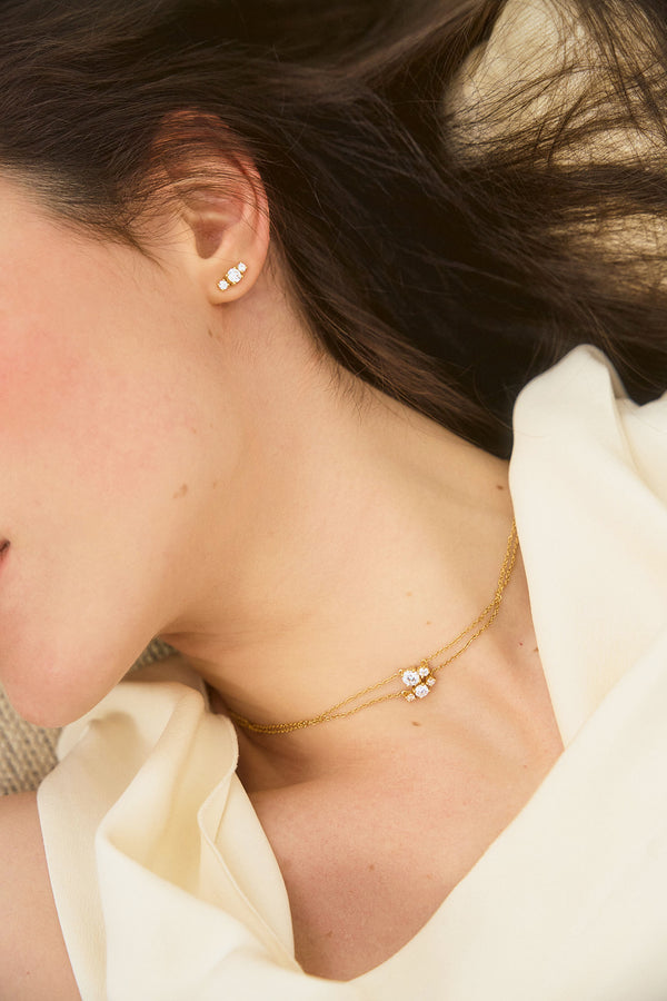 Woman wearing two yellow gold necklaces and earrings set with three diamonds, from the Essential collection by Nayestones. Fine, luminous jewelry worn on bare skin in natural light. Nayestones