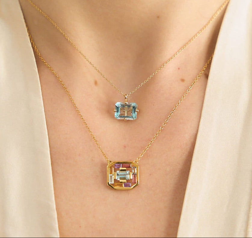 Model's neck wearing two 18K yellow gold necklaces from Nayestones, Belgian fine jewelry. The first is the Octogone Necklace featuring a big octogonal blue topaz, and the second is the Art Deco Aura Necklace, featuring a central octogonal blue topaz surrounded by baguette-cut tourmalines, citrines, amethysts and blue topaz. 