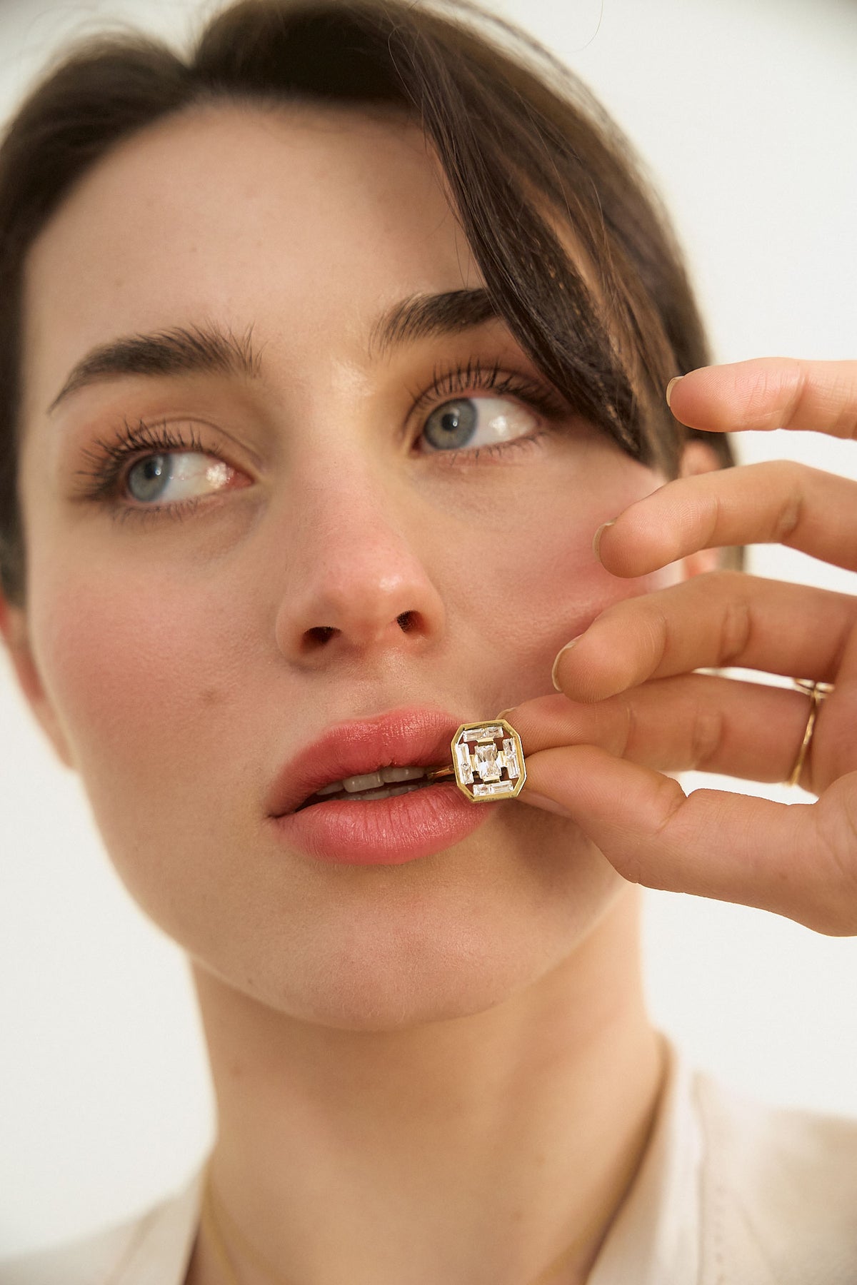 Woman's hands holding a ring to her mouth from the Art Deco collection, with a superb octagonal diamond in the center, surrounded by a row of baguette-cut diamonds. By Nayestones, Belgian fine jewelry.