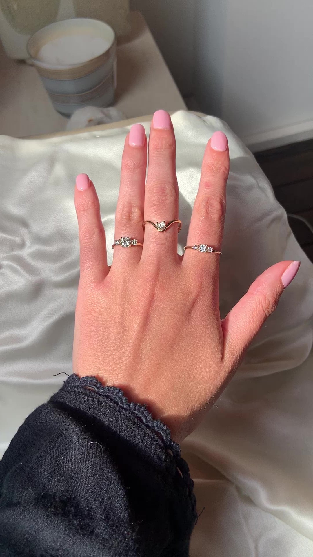 Hand wearing a 0.50 ct diamond, a 0.75 ct diamond trilogy engagement ring, and a heart ring, by Nayestones, Belgian fine jewelry.