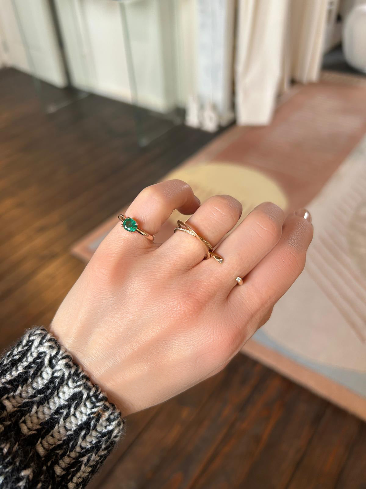 Woman's hand wearing three rings from Nayestones, the Gaia Emerald ring in 18K pink gold featuring a central oval emerald, the Full Moon ring and the moon Ellipse Pavé ring both featuring diamonds.
