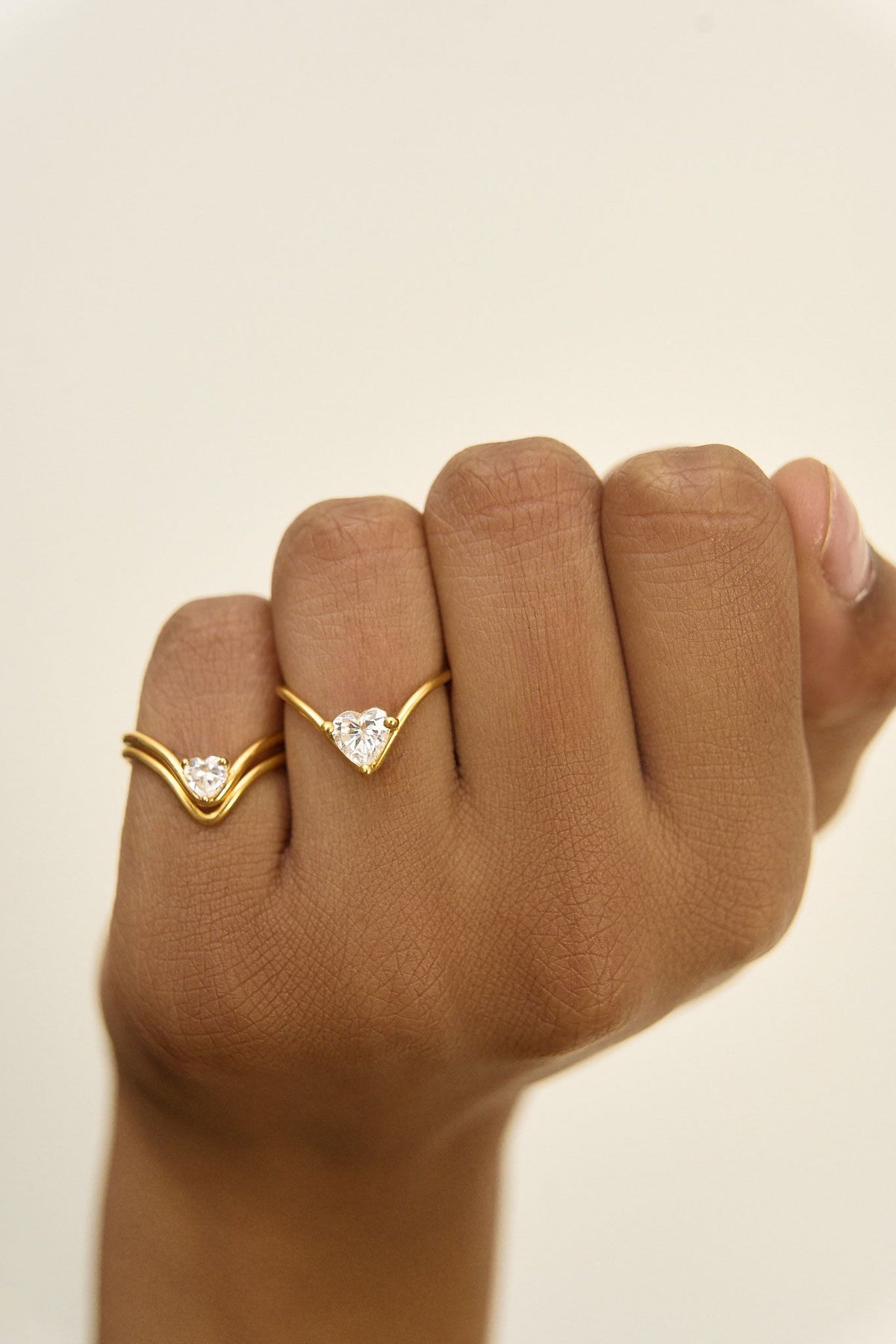 Model's hand wearing two heart diamond rings with different diamond carats, one stacked with a heart ring
