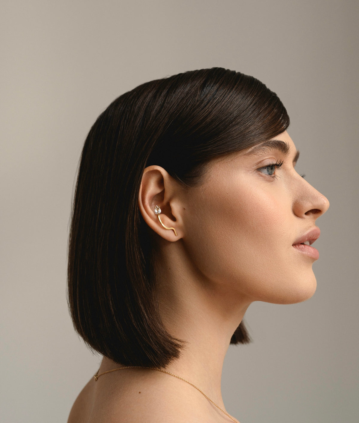 Model's head from profile, wearing on her ear the Lina Big Earring in 18K yellow gold with a pear-cut white topaz stone by Nayestones, Belgian fine jewelry. 