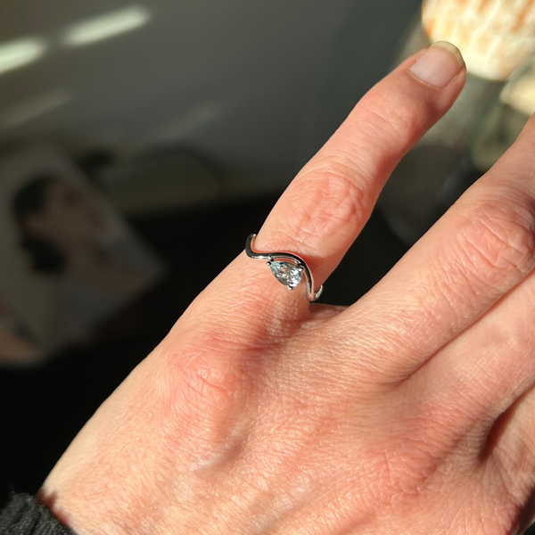Woman's hand wearing a ring on her pinky finger, from the Petite Comète collection by Nayestones, Belgian fine jewelry, in 18K white gold with a pear-shaped horizontal aquamarine in the center. Nayestones