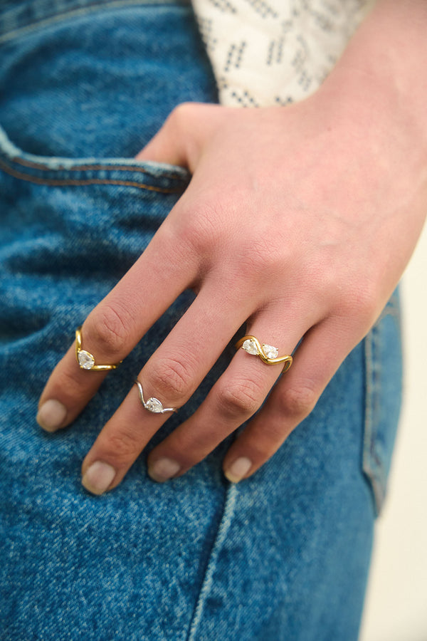 Hand resting on jeans wearing 3 rings from the Petite Comète collection by Nayestones on different fingers. The three rings are in 18K, yellow and white gold, and are set with 0.25 and 0.7 carat pear-shaped diamonds. Nayestones