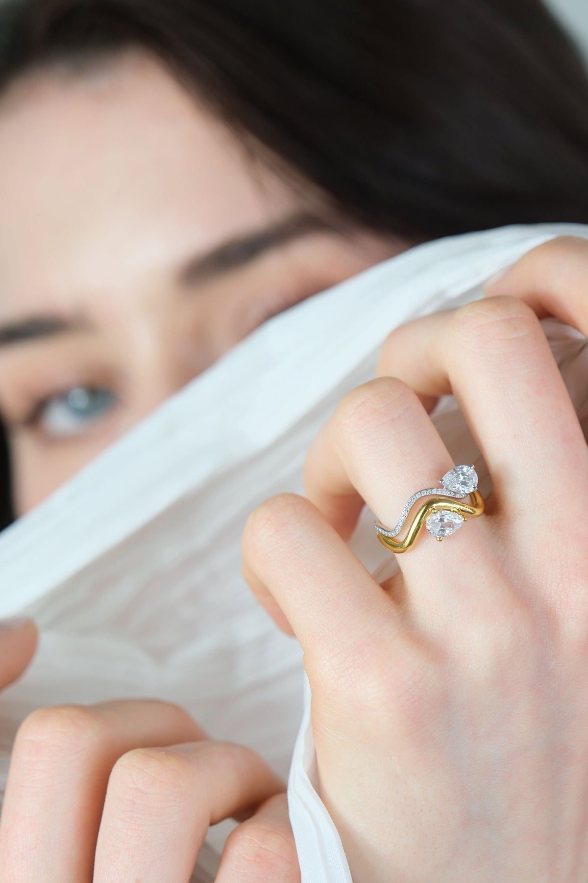 Model's hand with 2 rings from the Petite Comète collection on her ring finger, one in 18K white gold paved with diamonds, and the other in 18K yellow gold with thicker metal. Both rings are set with a 0.7-carat pear-shaped diamond.