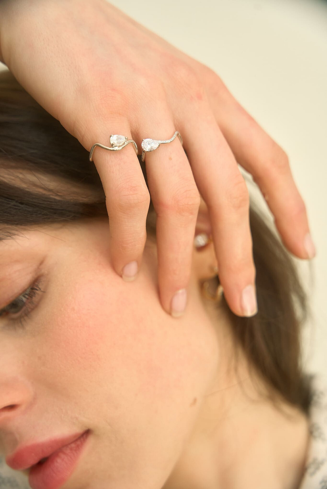 Une main féminine porte une bague en or blanc 18 carats ornée d'un diamant horizontal en forme de poire de 0.25 carat, et une bague en or blanc pavée de diamants avec un diamant central de 0.7 carat. L'atmosphère est naturelle et lumineuse, reflétant le minimalisme et l'élégance moderne de Nayestones.