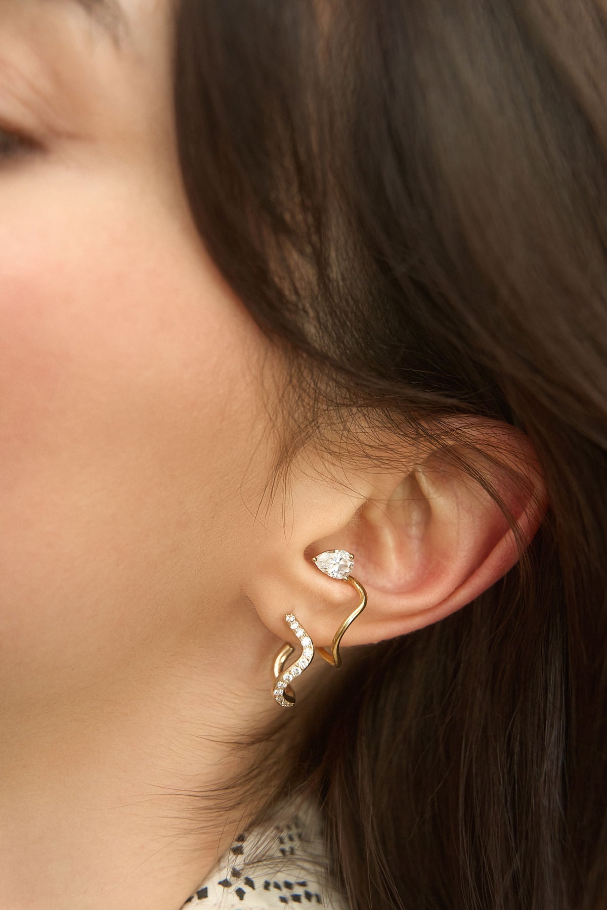 Woman's earpiece wearing an 18K gold earring paved with diamonds and a yellow gold earcuff set with a pear-cut diamond, from the Petite Comets collection by Nayestones.