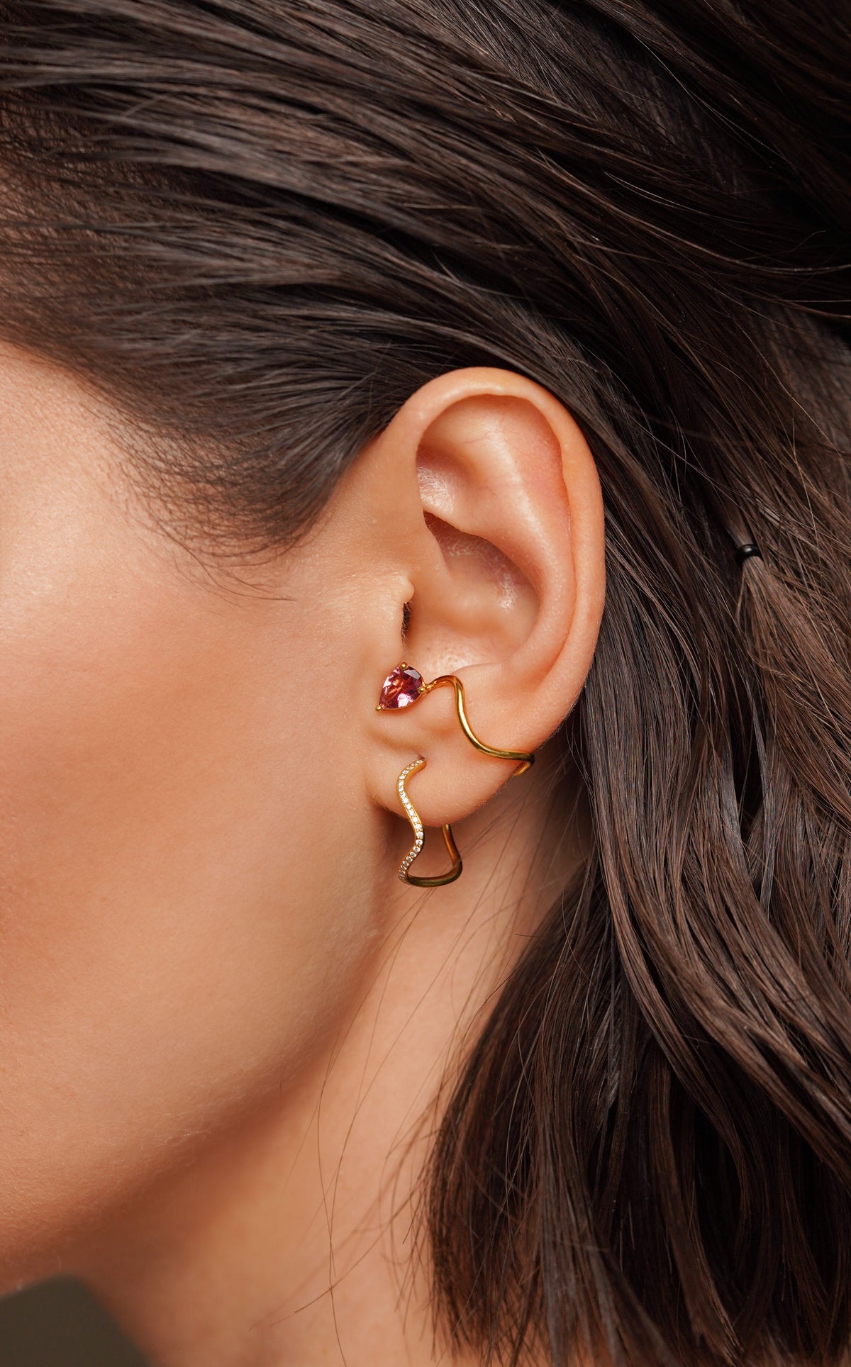 Woman's earpiece wearing an 18K gold earring paved with diamonds and a yellow gold earcuff set with a pear-cut pink tourmaline, from the Petite Comets collection by Nayestones.