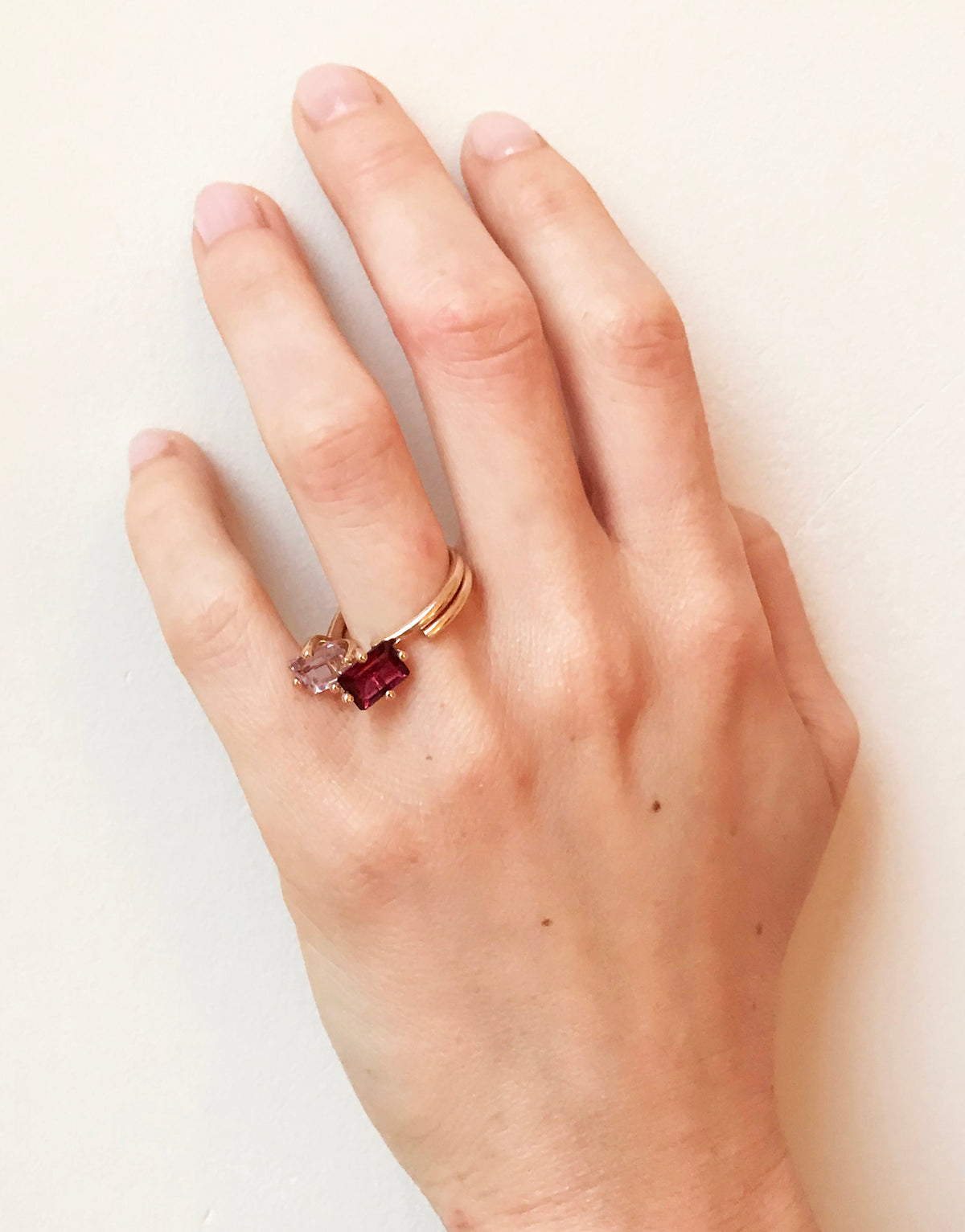Hand wearing two Signature Octogone engagement rings in 9k yellow gold with an octagon-cut amethyst and one with an octagon-cut rhodolite by Nayestones, Belgian Fine Jewelry.