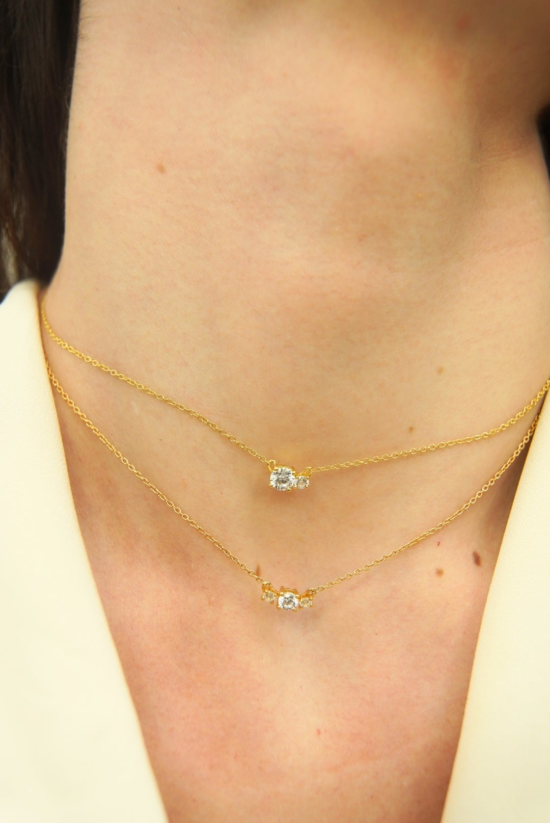 Woman wearing two yellow gold necklaces set with two and three diamonds of different sizes, from the Essential collection by Nayestones. Fine, luminous jewelry worn on bare skin in natural light.
